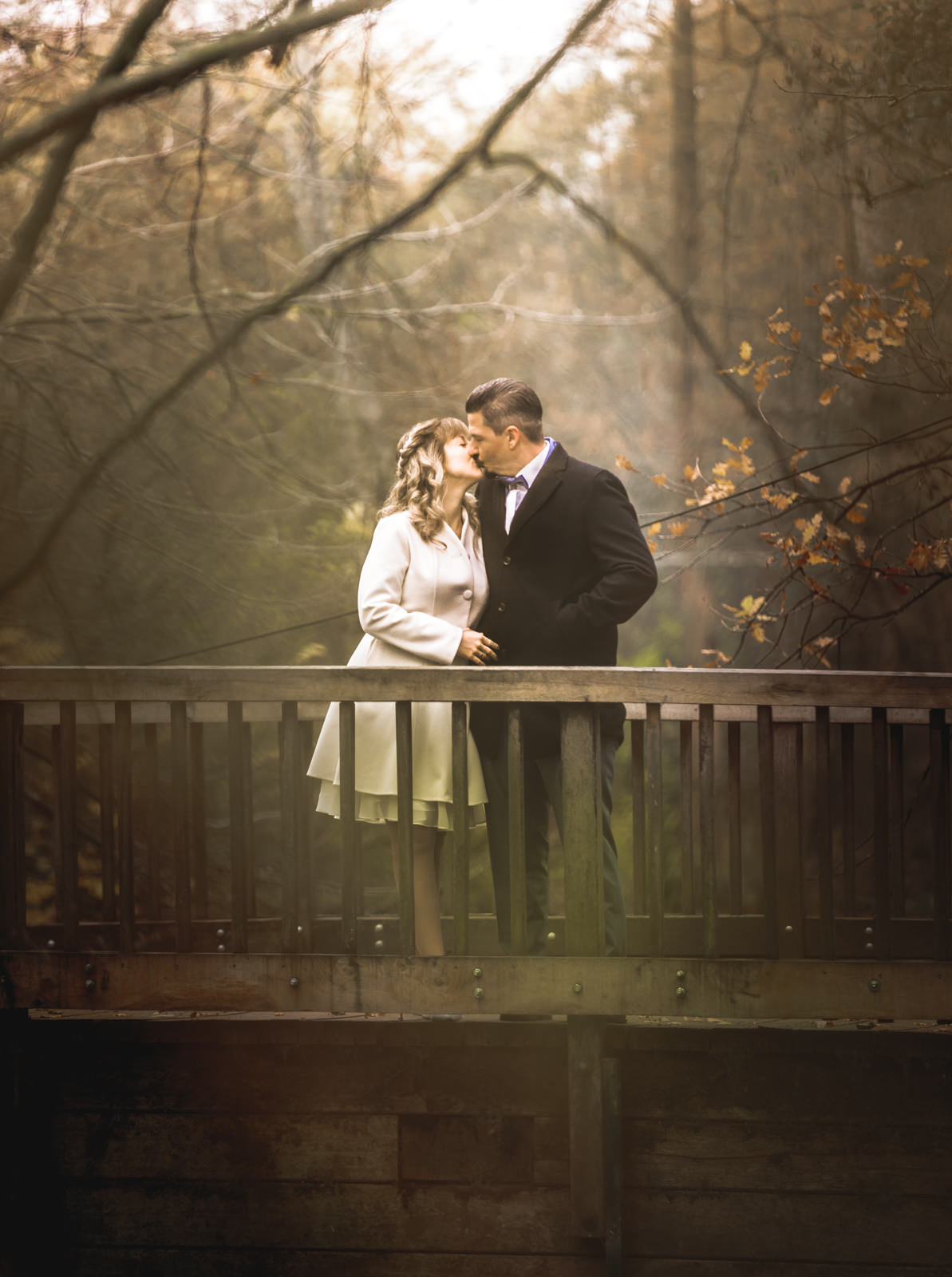 Brautpaar im Nebel küsst sich auf einer Brücke